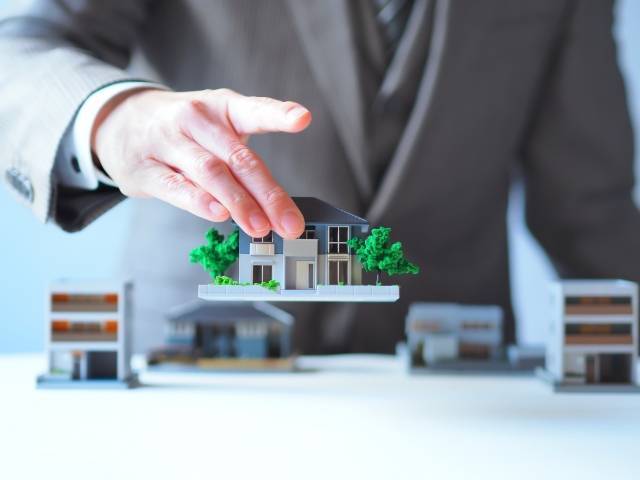 家の模型を持ち上げる人物